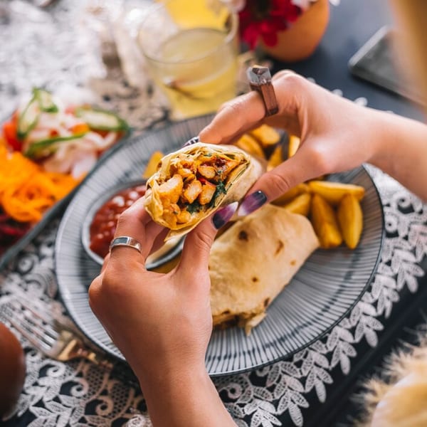 Hands holding a Chinese chicken wrap filled with vegetables, served with fries and sauce.