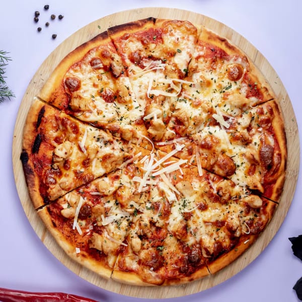 A sliced chicken pizza with melted cheese and herbs on a wooden board.