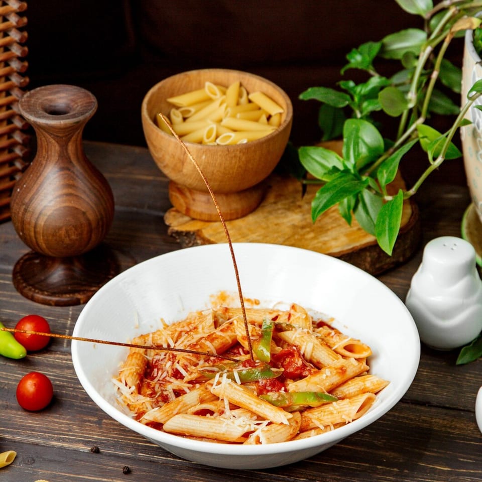 Penne pasta with red sauce, green peppers, and cheese in a white bowl.