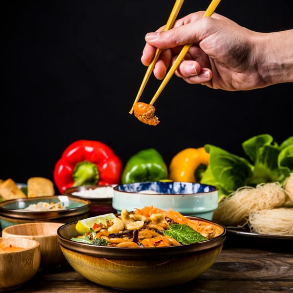 A hand uses chopsticks to pick up a piece of Chinese food from a bowl of stir-fry.