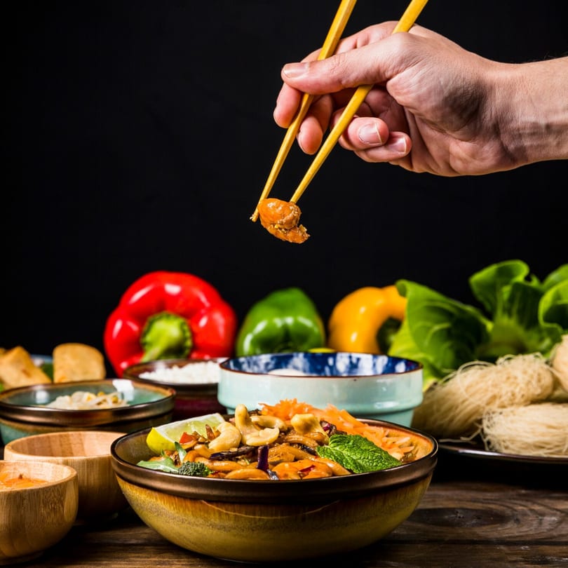 A hand uses chopsticks to pick up a piece of Chinese food from a bowl of stir-fry.