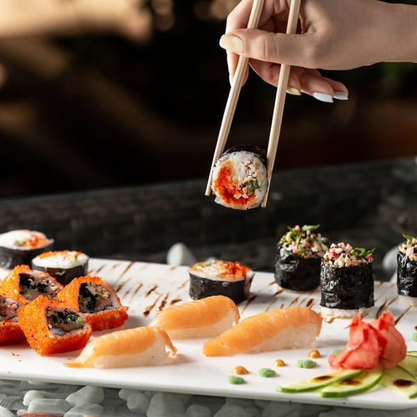 Chopsticks hold a sushi roll above a white plate filled with various sushi and sashimi.